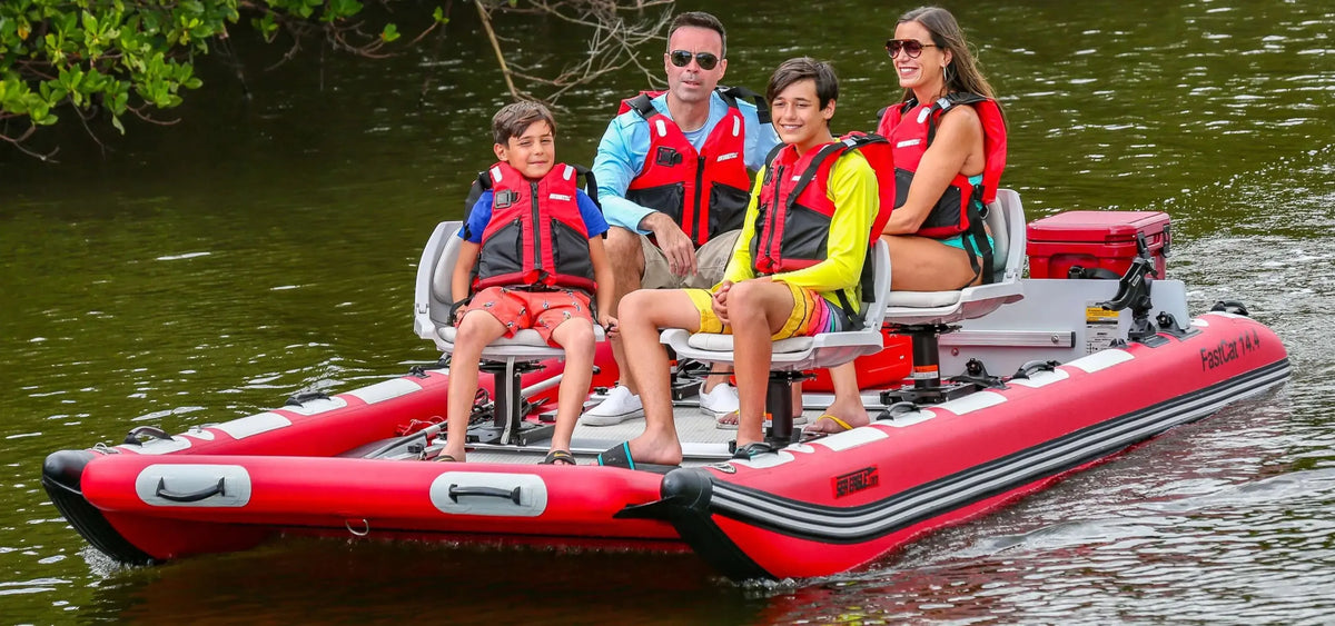 Family of four in red Sea Eagle FastCat14™ inflatable catamaran boat on water.