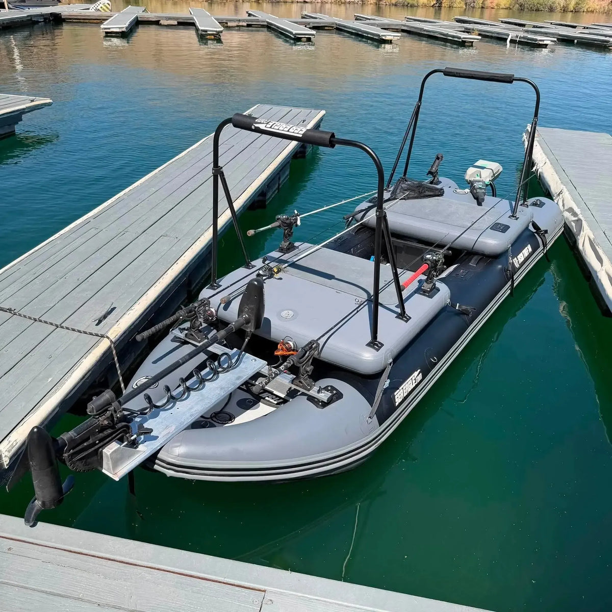 A gray sea eagle inflatable boat with black handles and rigging, docked at a wooden pier in green water.