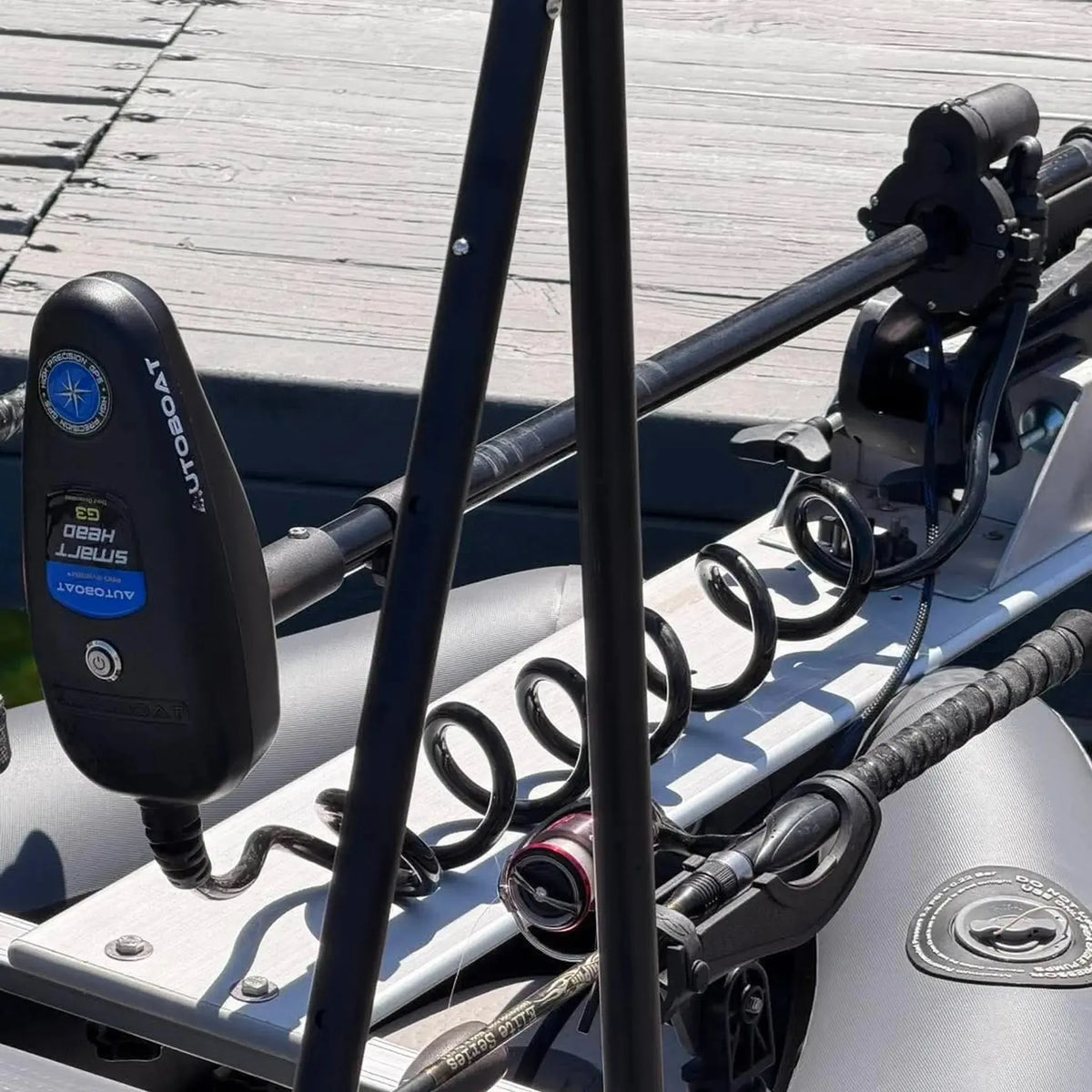 Close-up of a black Autopay HydroLift electric trolling motor mount and controller on a white boat transom, with black mounting poles and coiled hoses.