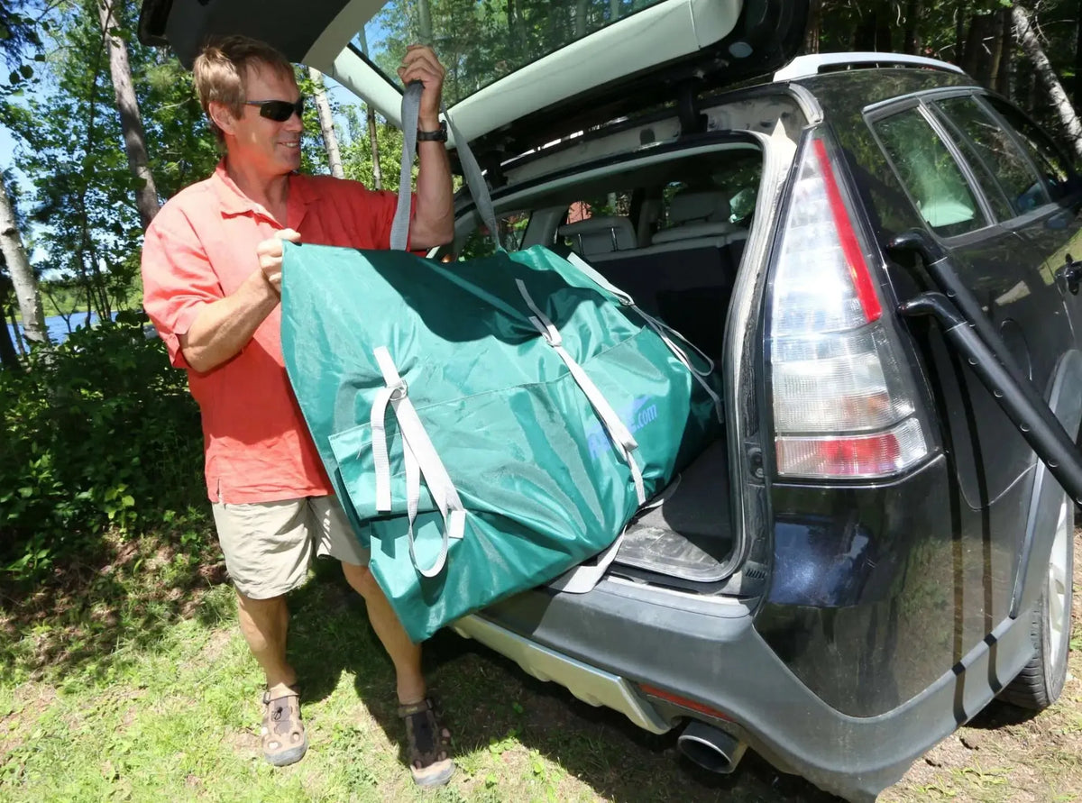 Man in sunglasses loading a compact, dark green Sea Eagle TC16 inflatable canoe bag into a car trunk.
