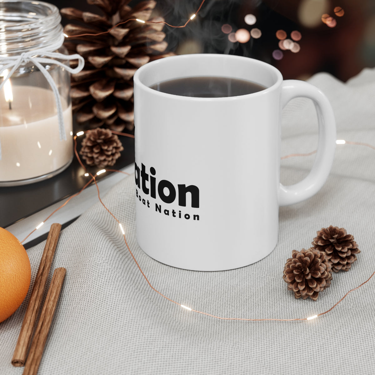 White mug with 'TBNation' text on a table with decorative items including a candle, oranges, and pine cones.