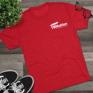 Red t-shirt with 'TBNation' logo on a wooden surface with sneakers and a plant.