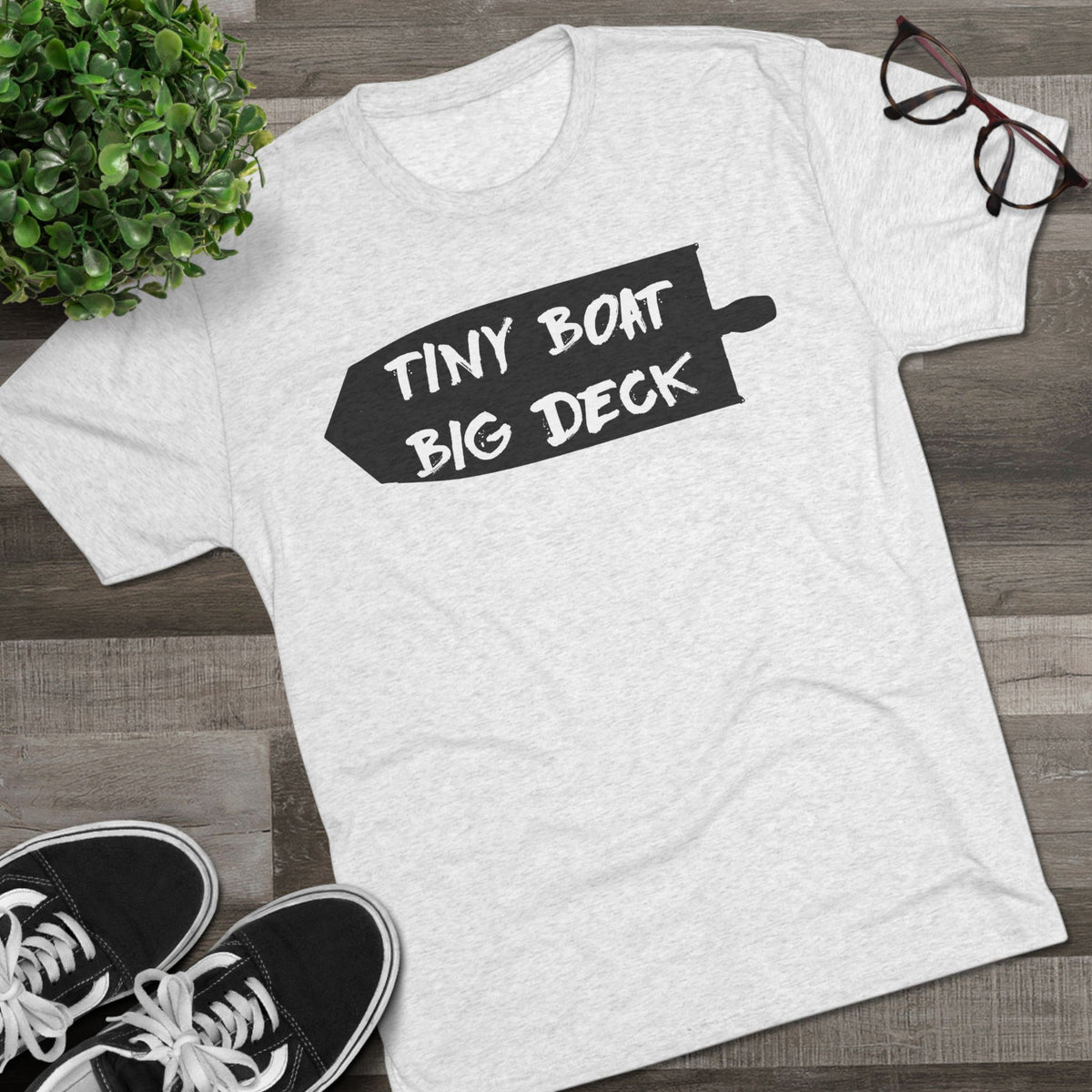 White t-shirt with 'Tiny Boat Big Deck' text on a wooden surface with shoes and glasses.