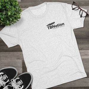 White t-shirt with 'TBNation' logo on a wooden surface with sneakers and glasses.
