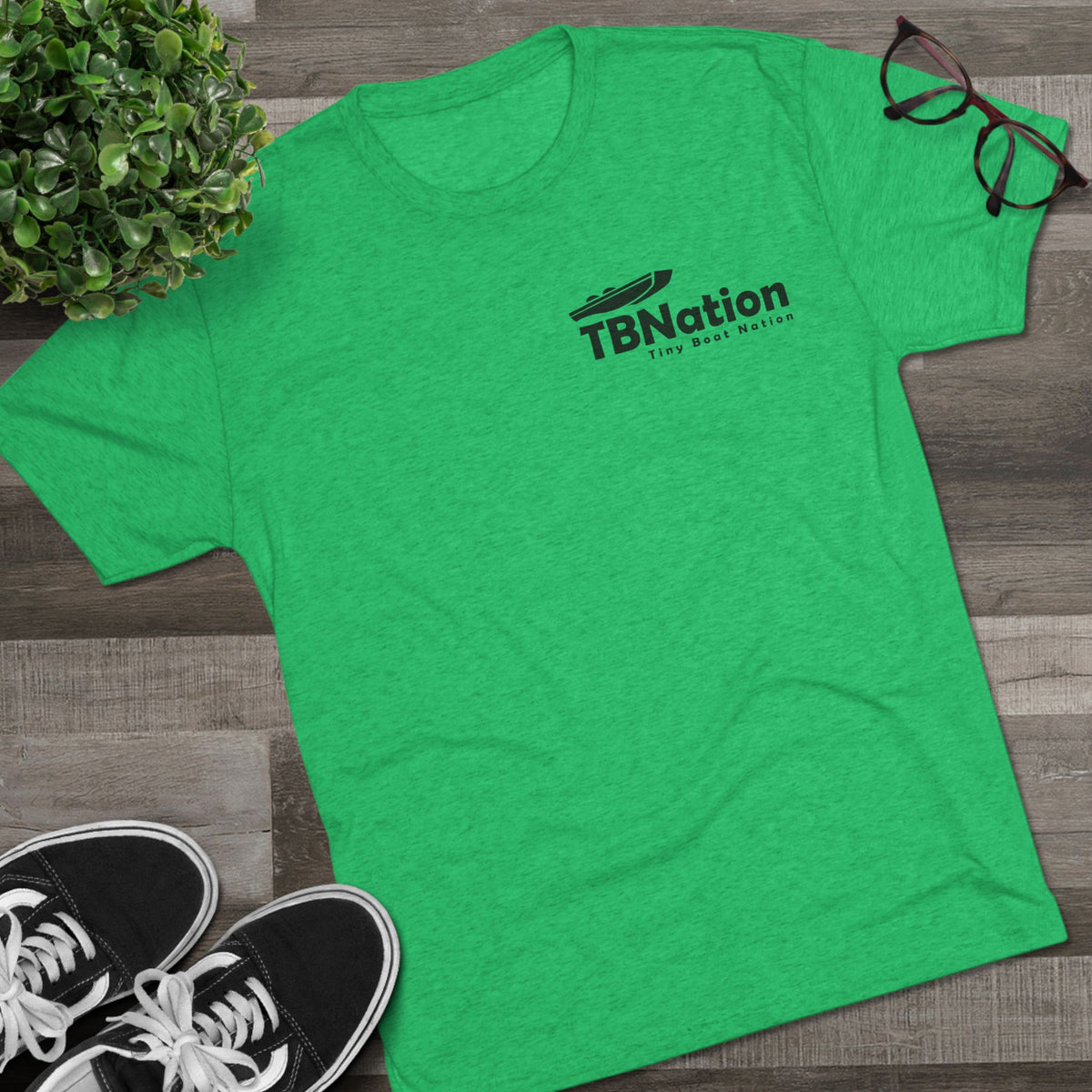 Green t-shirt with 'TB Nation' logo on a wooden surface with shoes and a plant.