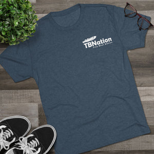 Blue t-shirt with 'TB Nation' logo on a wooden surface with sneakers and a plant.
