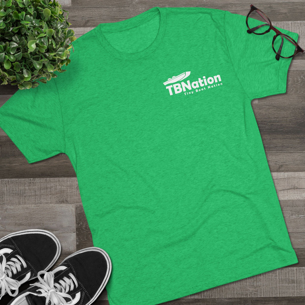 Green t-shirt with 'TBNation' logo on a wooden surface with shoes and glasses.