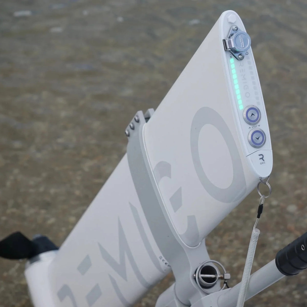 A macro shot of the top interface of the Remigo One electric outboard. It features a minimalist control panel with two arrow buttons, a magnetic kill-switch key, and a glowing green LED bar indicating battery life or power level.
