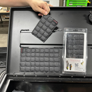 Hand holding a small black quilted Magnalure Pad above a larger one attached to a black surface, next to a packaged pad.