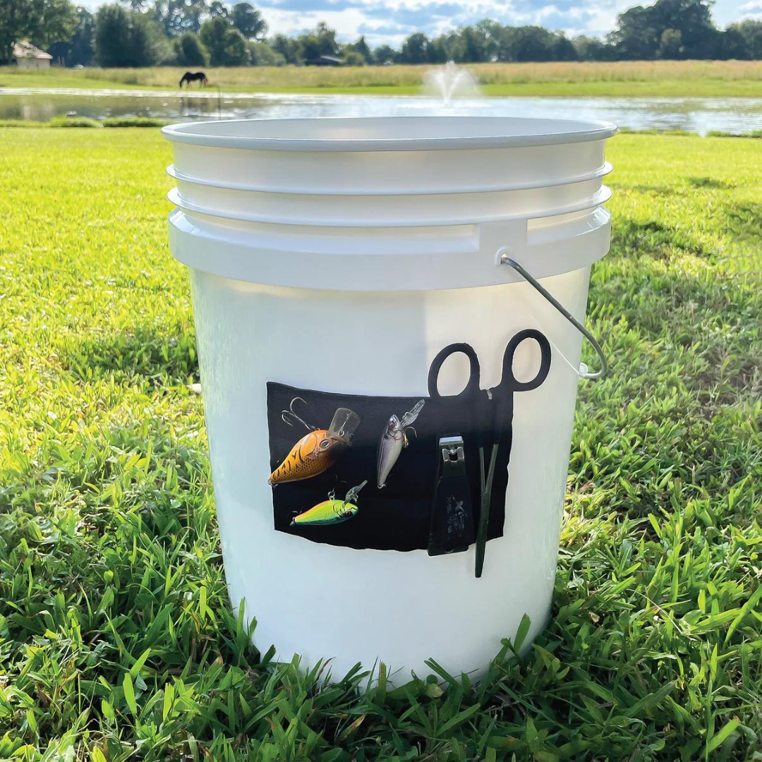 White fishing bucket with a black Magnalure Pad holding colorful lures, scissors, and a tool.