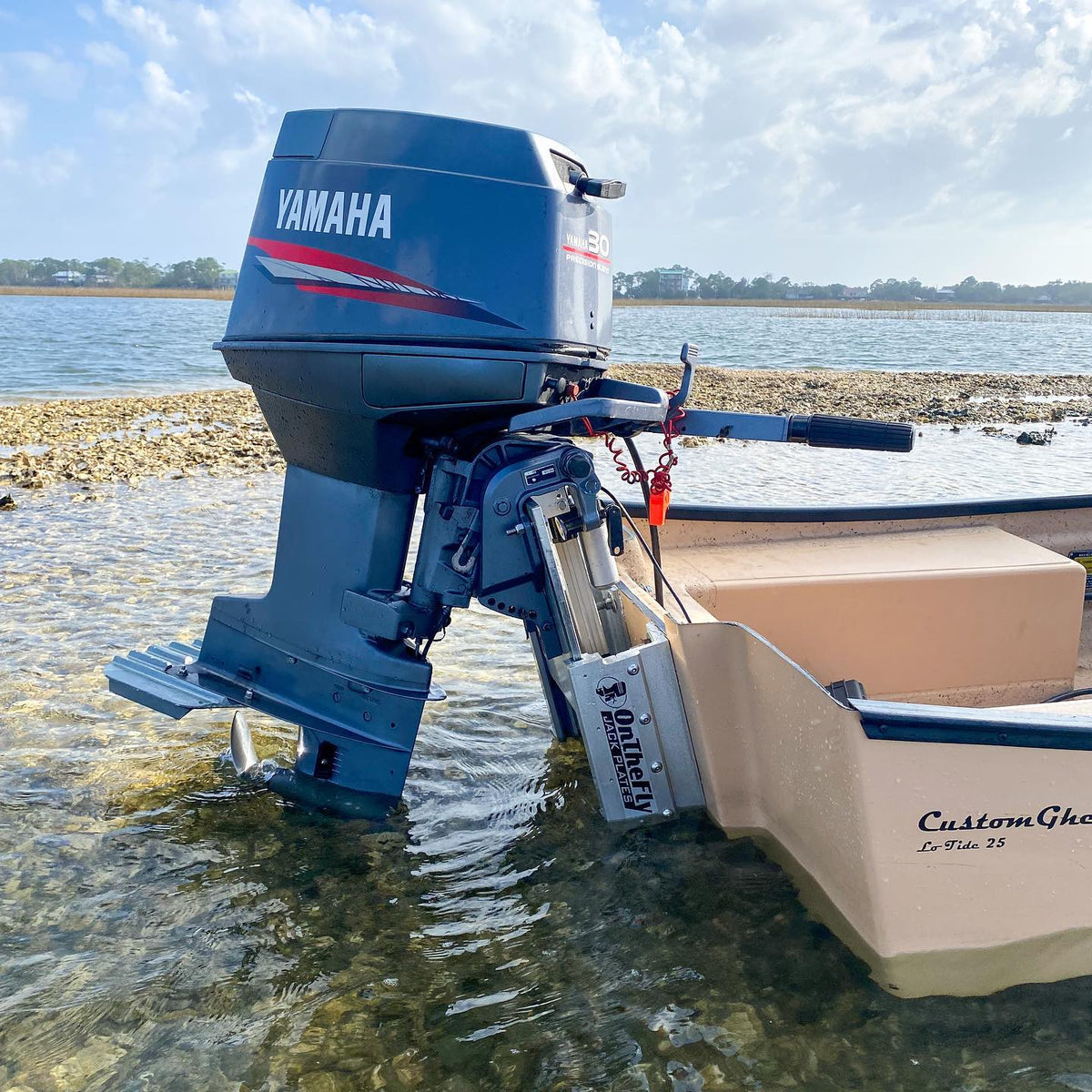 Silver OnTheFly manual jackplate installed on a tan boat with a Yamaha outboard motor in shallow water.