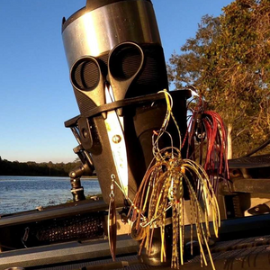 Black Railblaza DrinkHold with fishing lures and scissors attached, holding a silver thermos by a lake.