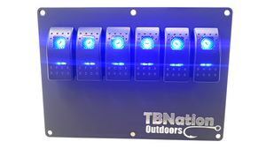 Black 6-gang TBNation Outdoors hydro-dipped aluminum switch panel with six glowing blue rocker switches.